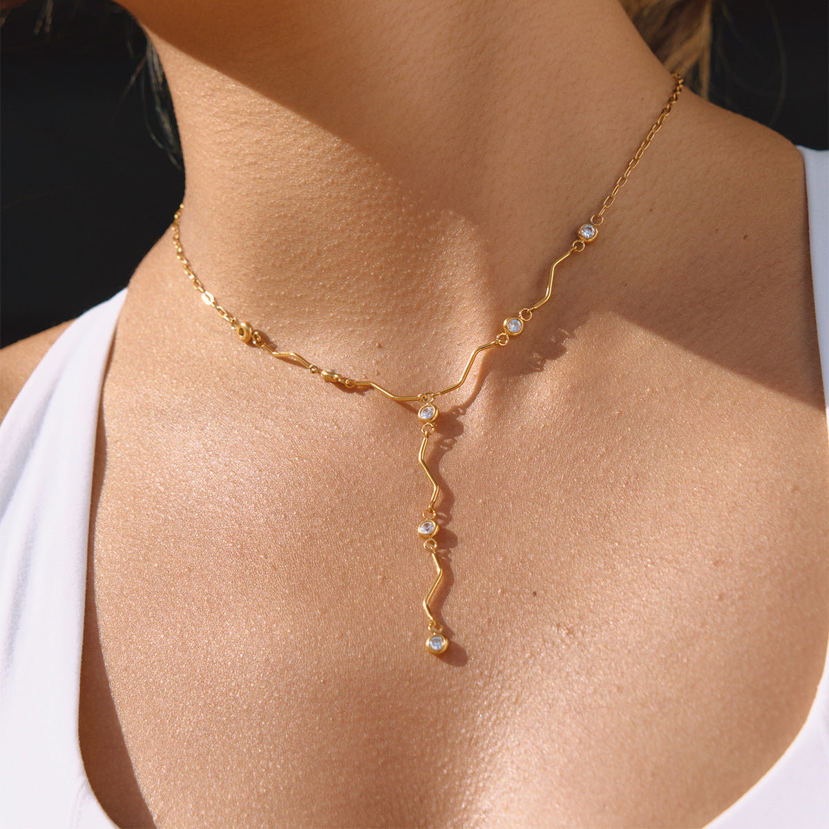 Woman wearing the Ondine wave crystal Y necklace in sunlight, the drop resting on her chest