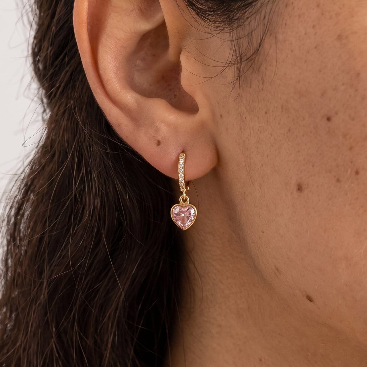 Woman wearing the Paola pink heart gold earrings on the ear