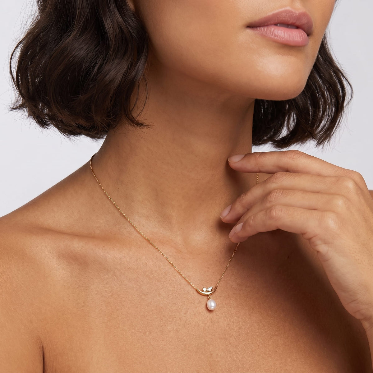 Woman wearing the Pauline moon pearl gold necklace at the collarbone while resting her hand near her chin