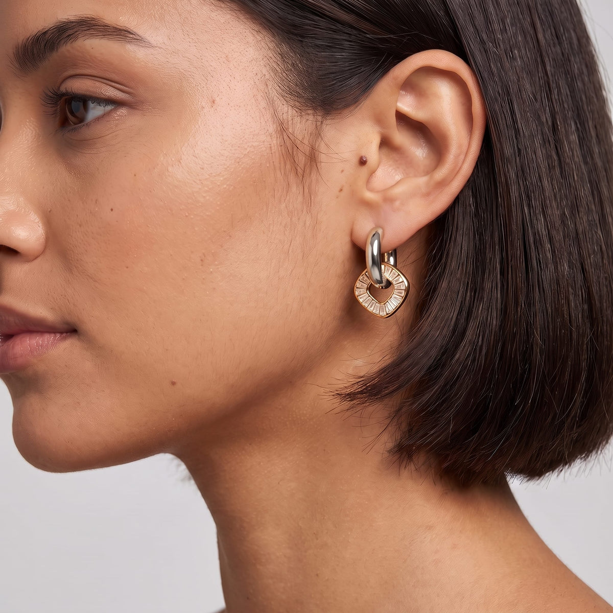 Woman wearing the Salomé baguette charm two-tone earrings on her ear against a plain studio background