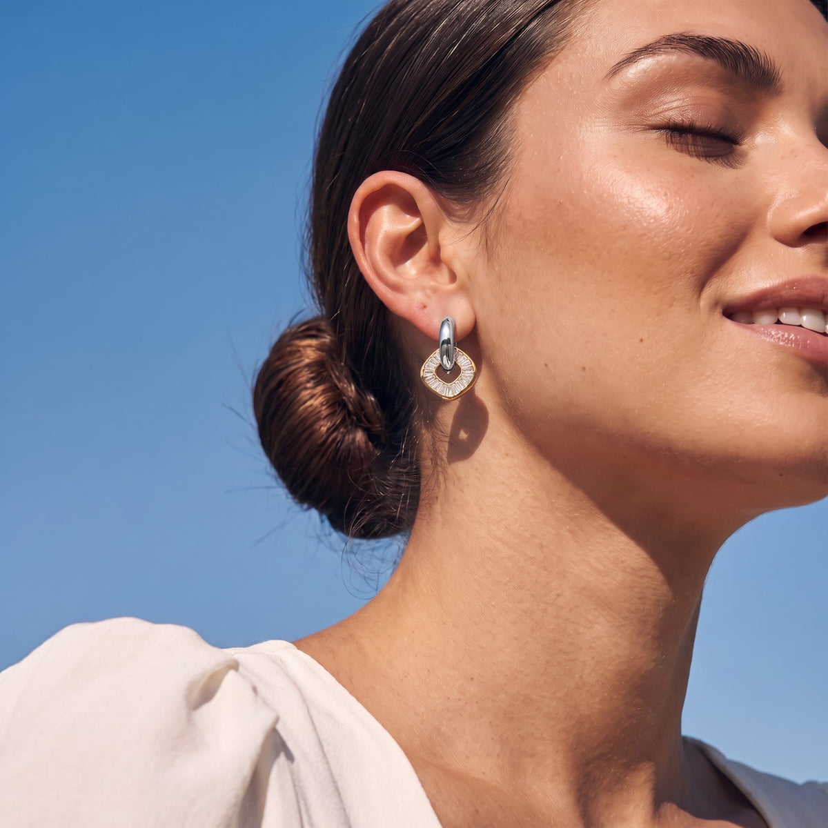 Woman wearing the Salomé baguette charm two-tone earrings on her ear under bright blue sky
