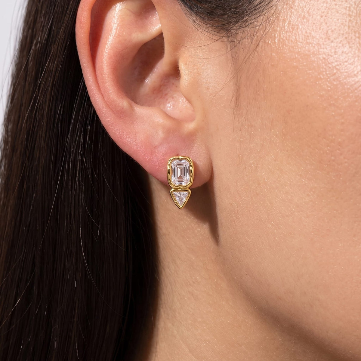 Woman wearing the Sidonie emerald-cut crystal gold earrings on her earlobe, close up