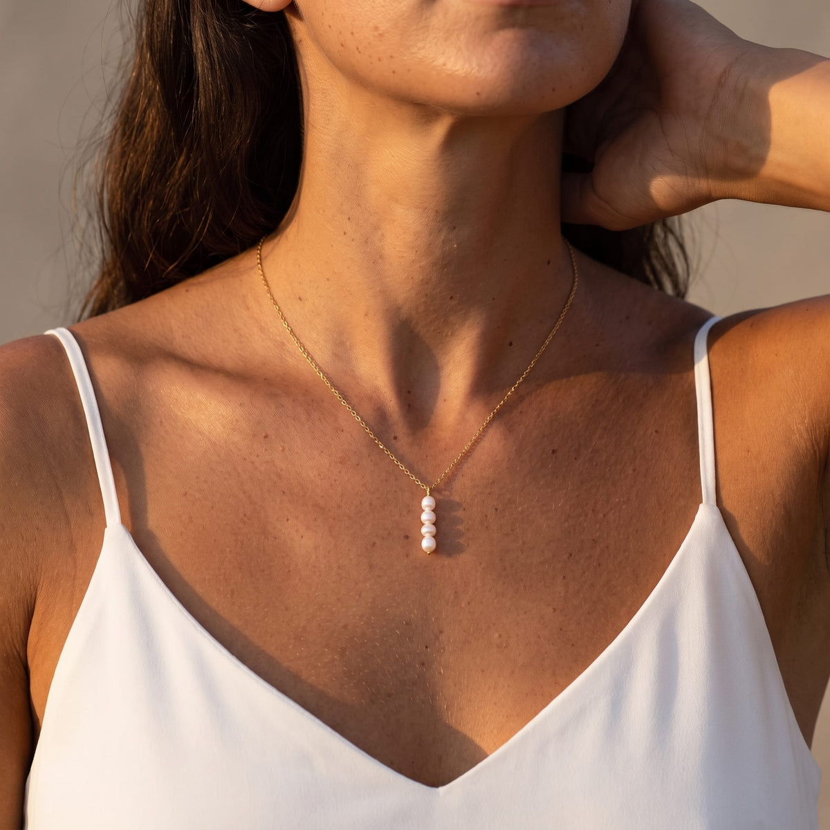 Woman wearing the Simone stacked pearl gold necklace at the collarbone in warm sunlight wearing a camisole