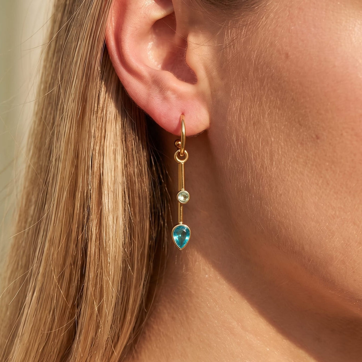 Woman wearing the Sixtine blue bar gold earrings on her earlobe in warm sunlight