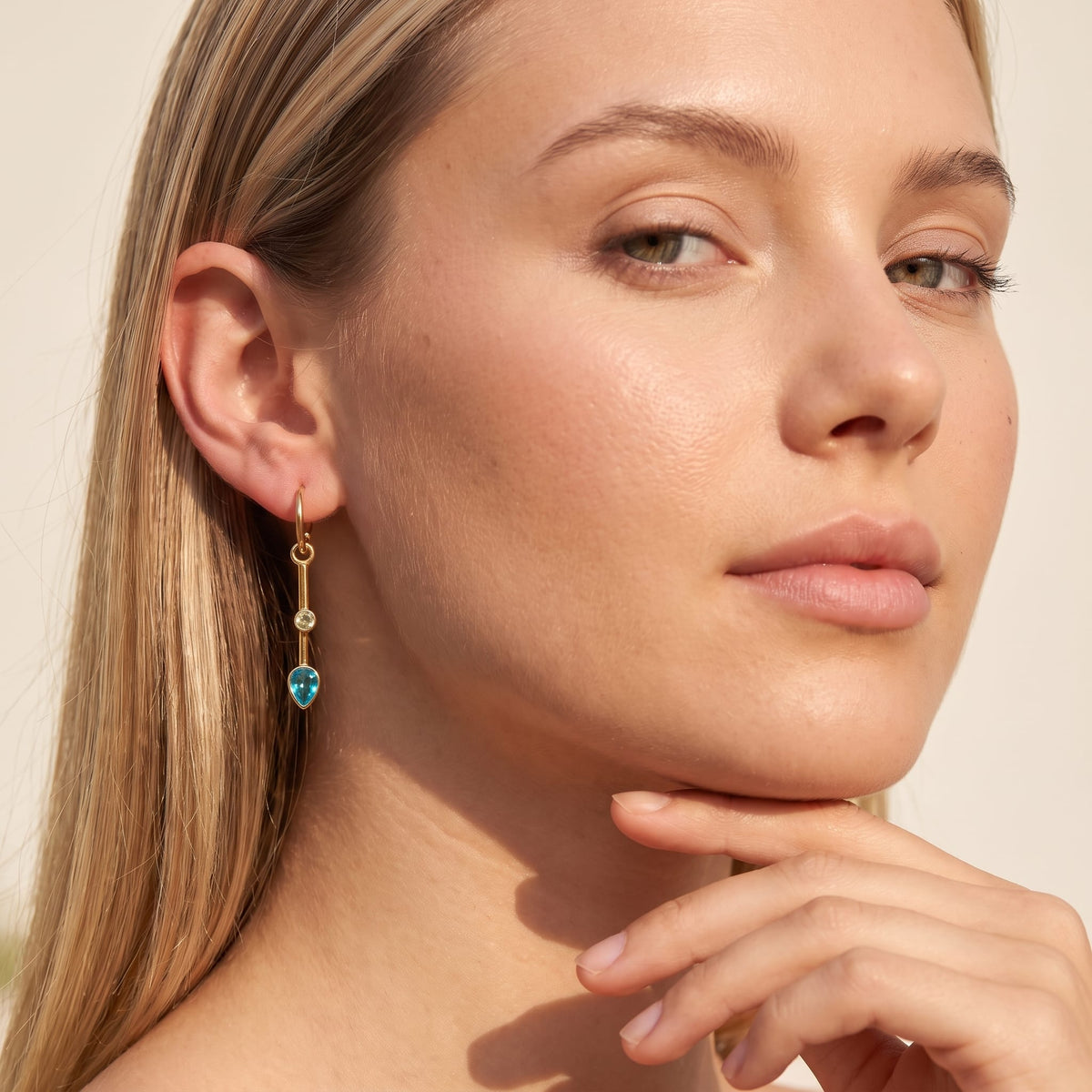Woman wearing the Sixtine blue bar gold earrings on her ear with hand resting on chin