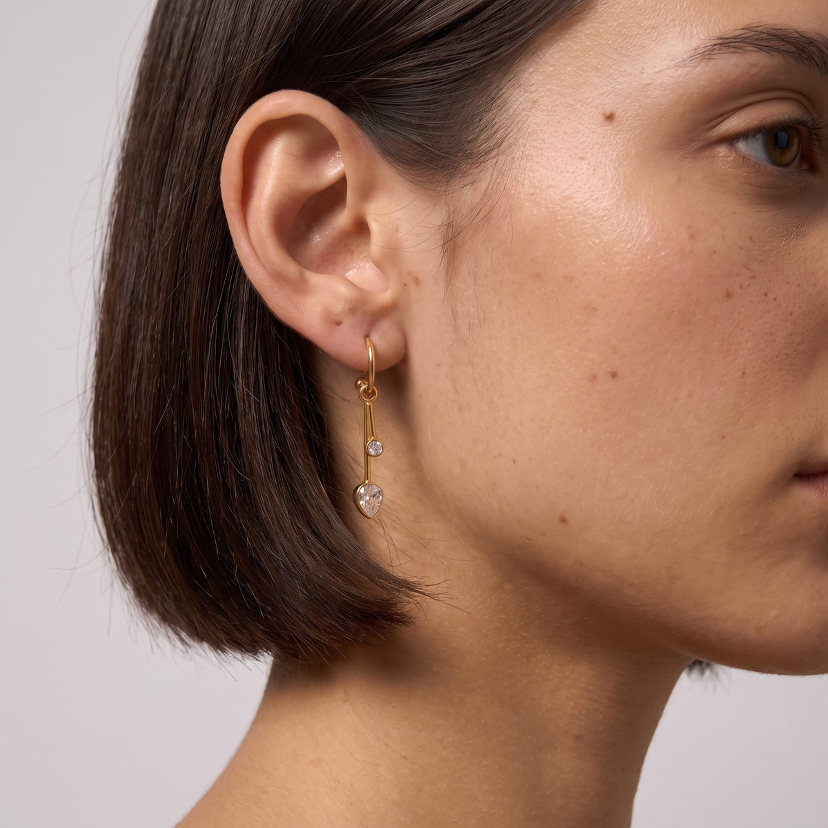 Woman wearing the Sixtine crystal bar gold earrings on her earlobe featuring short dark hair