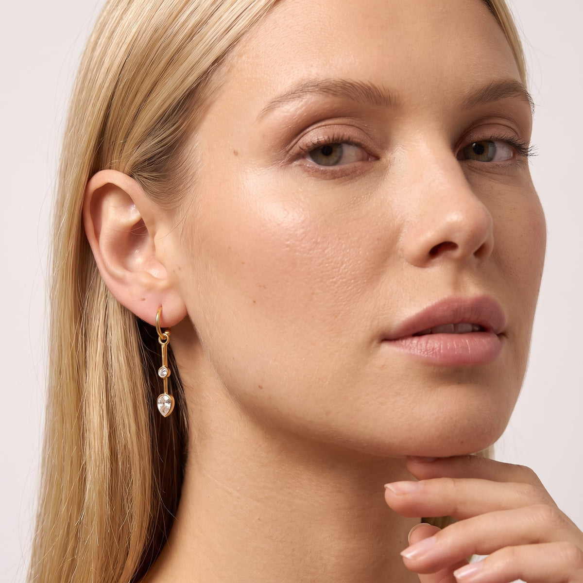 Woman wearing the Sixtine crystal bar gold earrings on her ear touching her chin gently