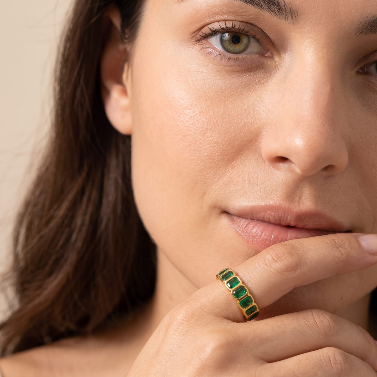 Woman wearing the Sophie green baguette gold ring on the hand touching her lips in a close-up