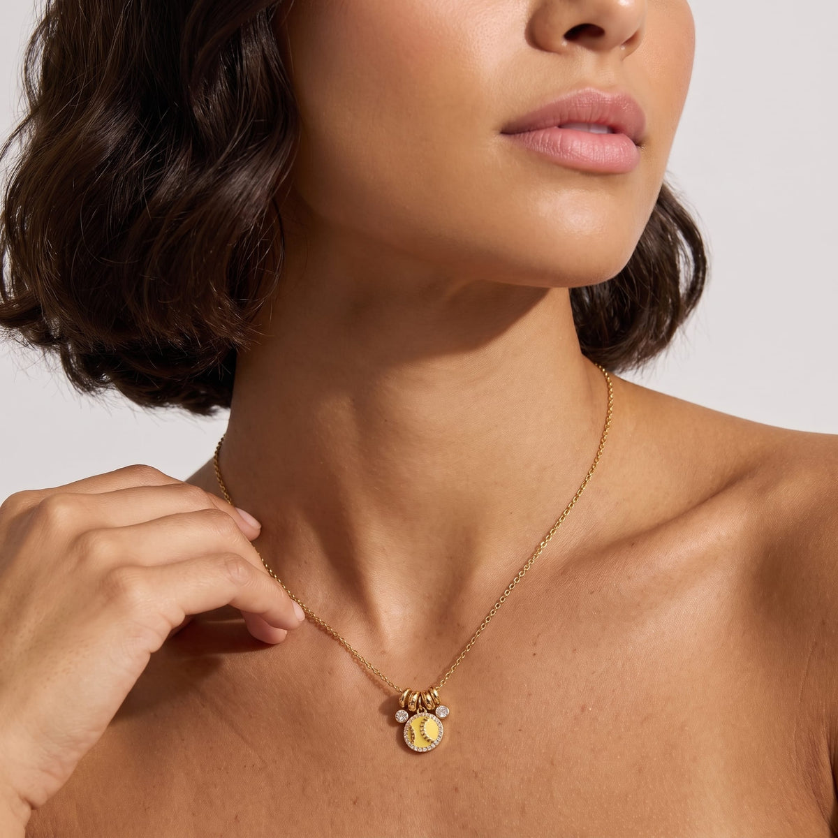 Woman wearing the Vida softball charm gold necklace at the collarbone with her hand near her neck