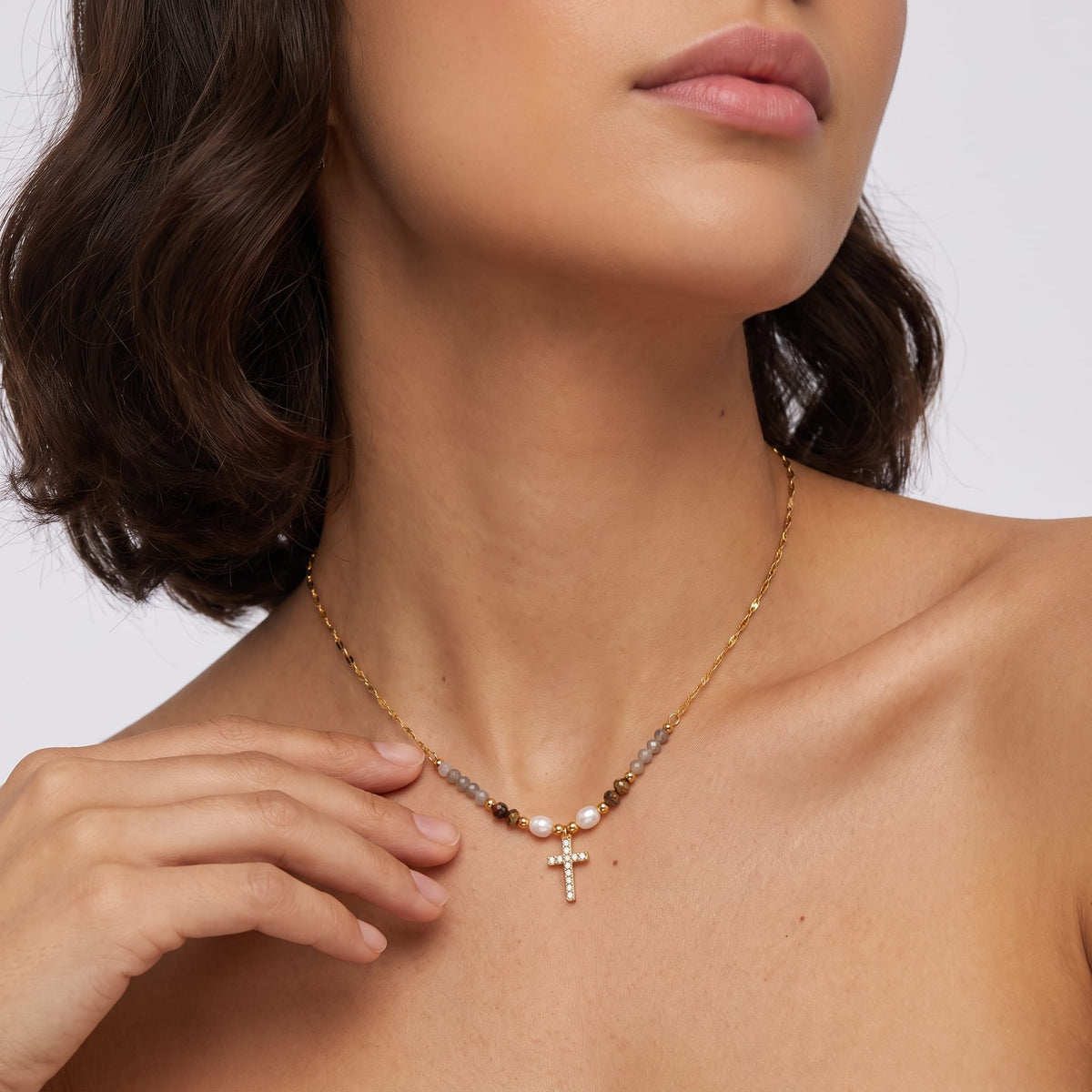 Woman wearing the Viola pearl cross gold necklace at the collarbone while touching the chain