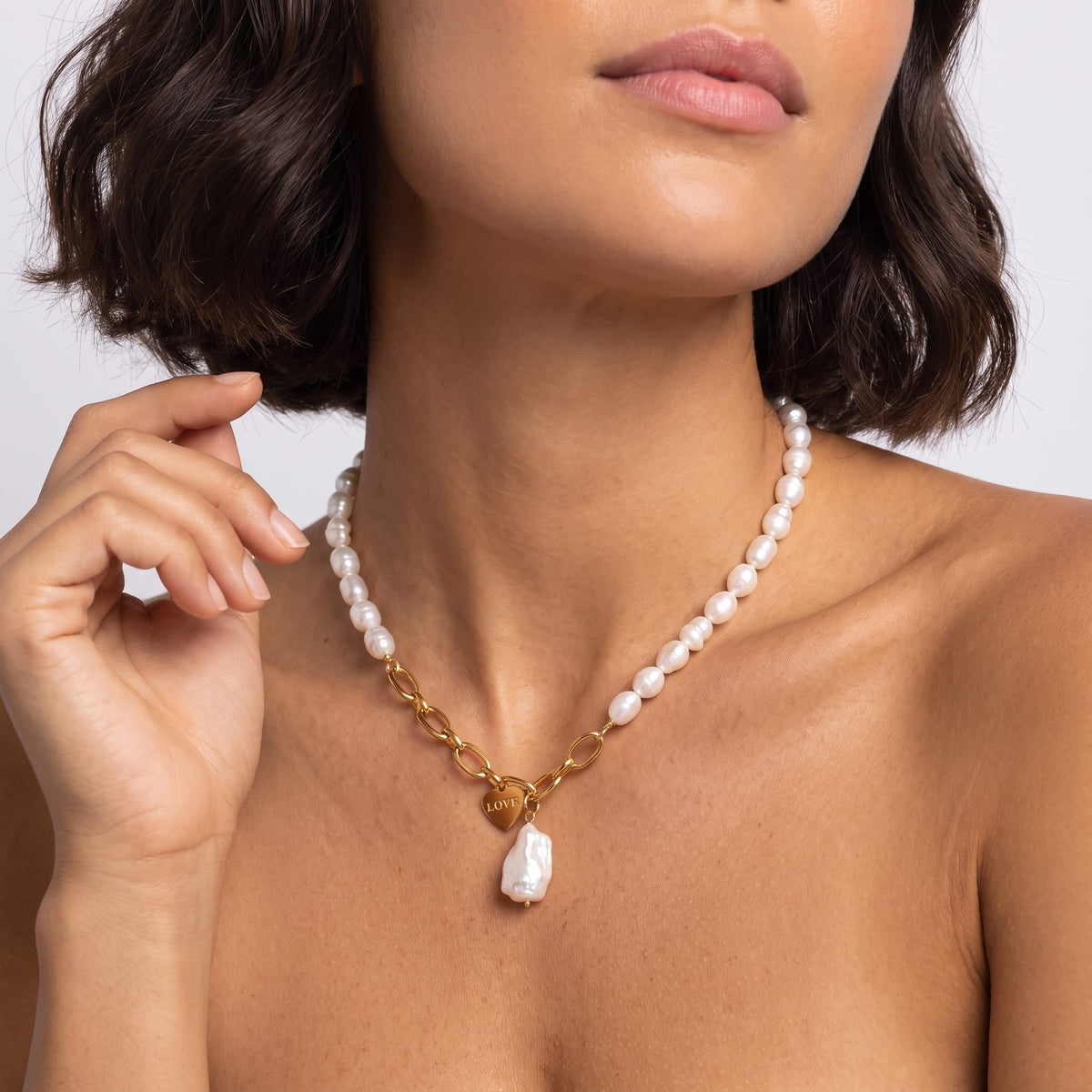Woman wearing the Vivienne pearl love gold necklace at the collarbone with her hand raised