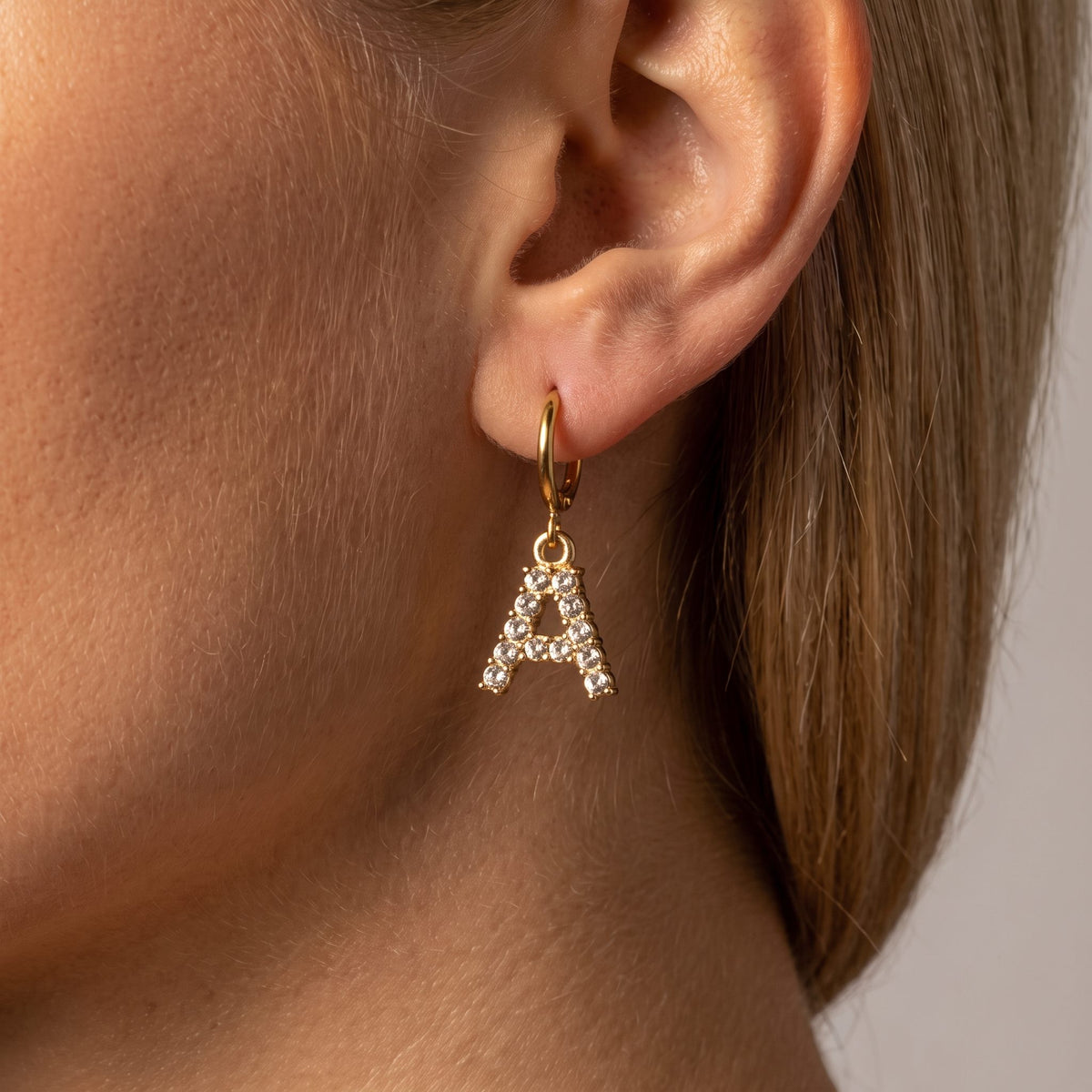 Woman wearing the Wilhemina crystal letter A charm on a small gold hoop