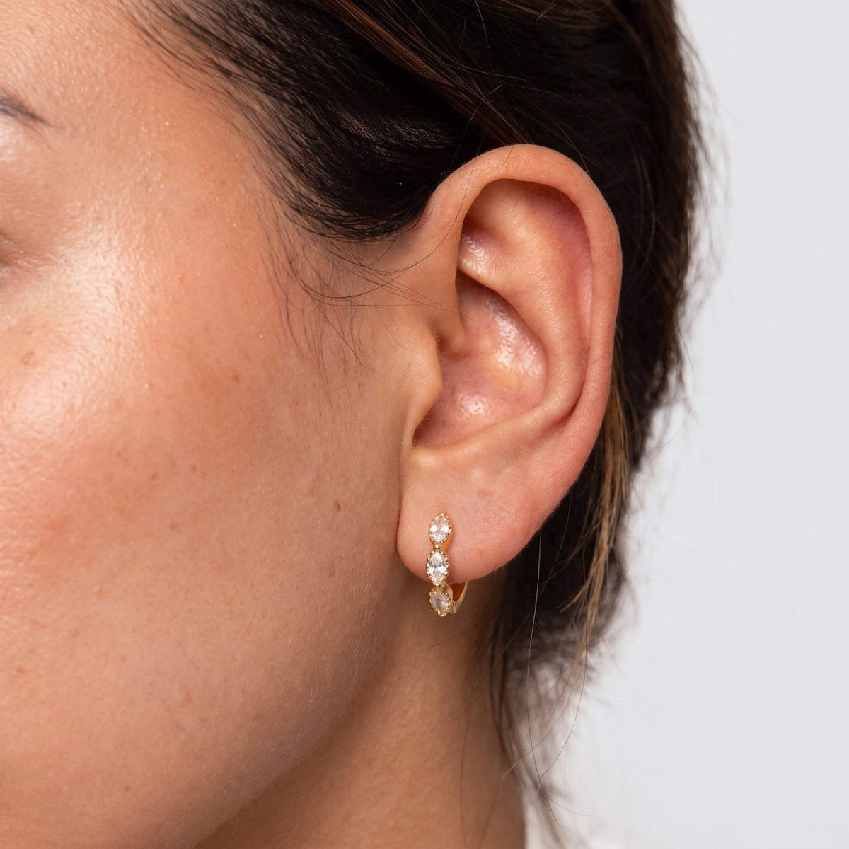 Wider view of a woman wearing the Zoé marquise huggie gold earrings on the ear