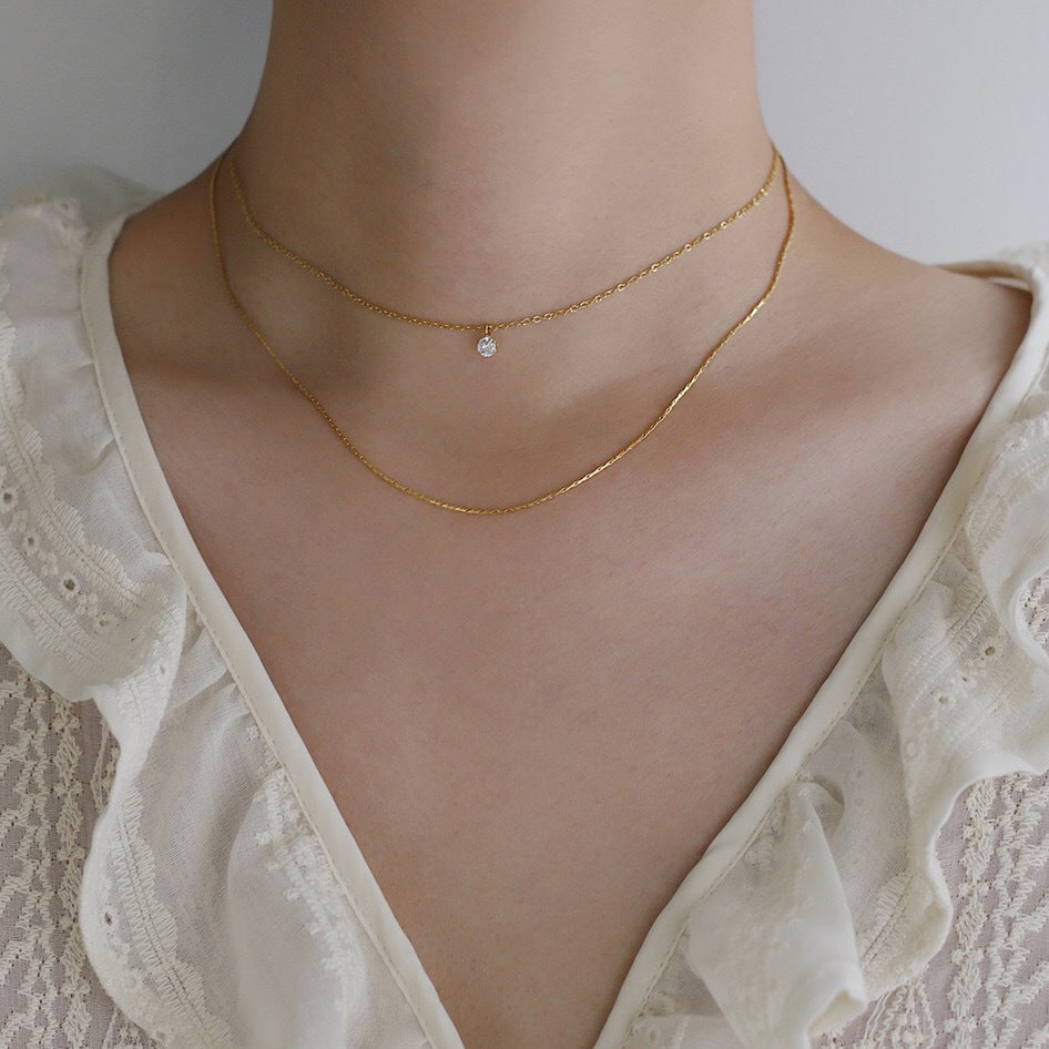 Woman wearing the Lora layered gold necklace with a small crystal on the short chain, a longer chain below