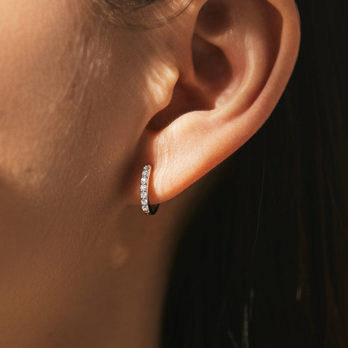 Woman wearing the Olivia pavé silver huggie, clear crystals glinting in warm side light