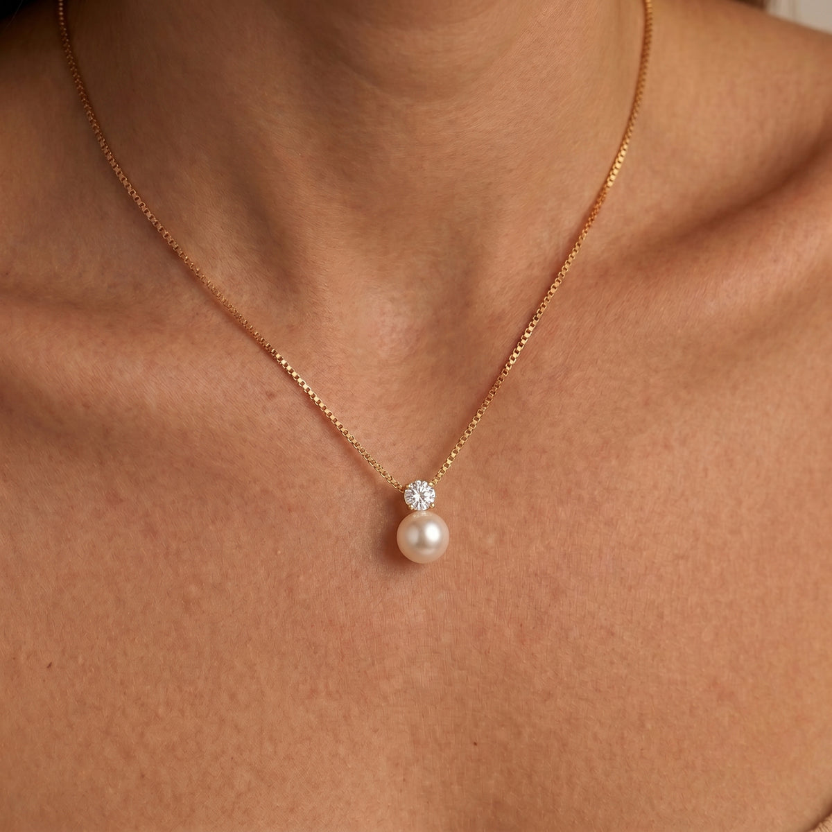 Woman wearing the Arianne gold box chain necklace, a round pearl hanging below a single crystal