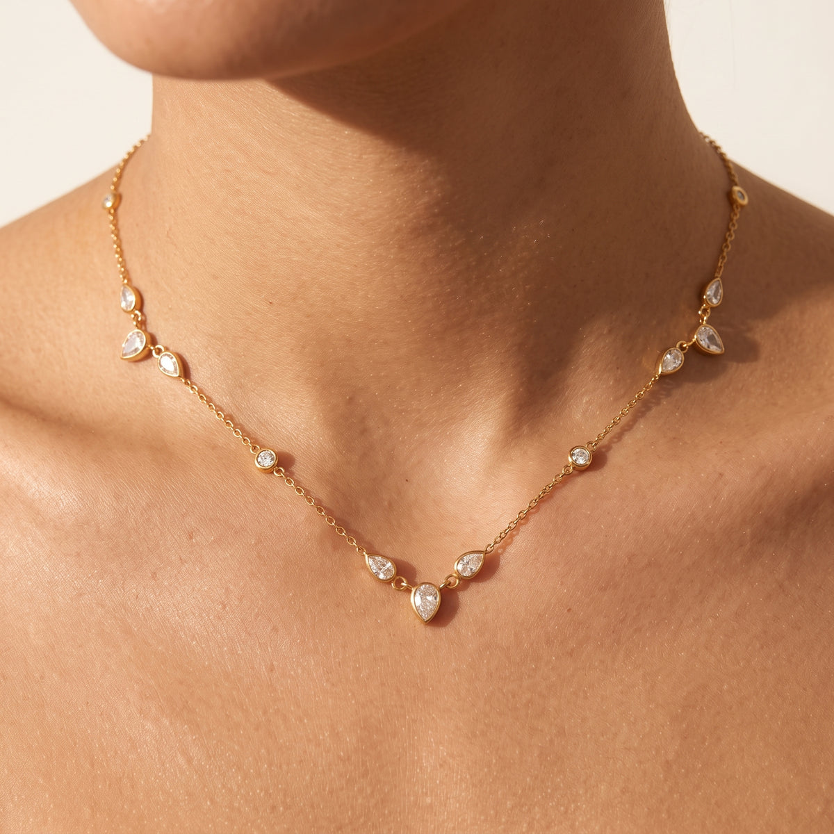 Woman wearing the Lucienne gold necklace lined with bezel-set pear and round crystals