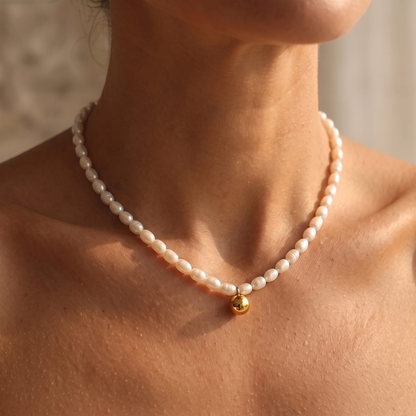 A close-up of a model wearing a delicate white pearl necklace with a small gold bead accent at the center, styled with a white strapless top.