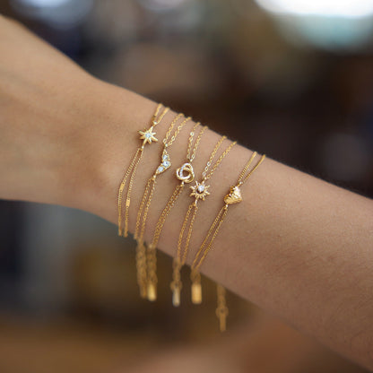 Hand wearing the Adèle heart bracelet in a stack of fine gold charm chains