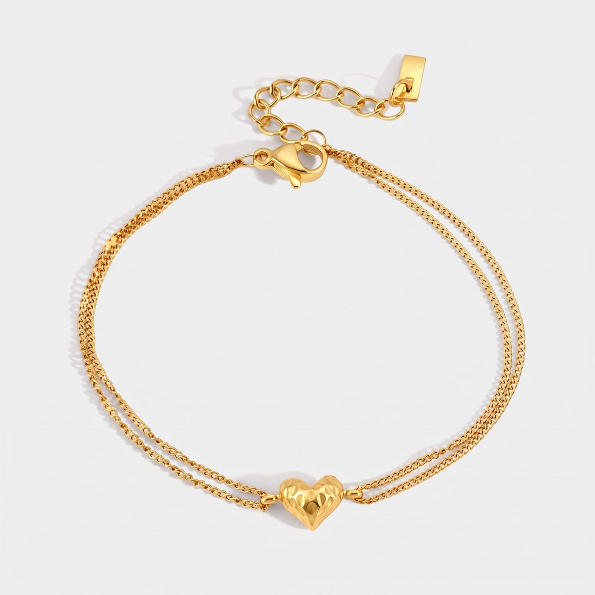 Adèle hammered heart gold bracelet on a plain white surface displaying its double fine chain clasp