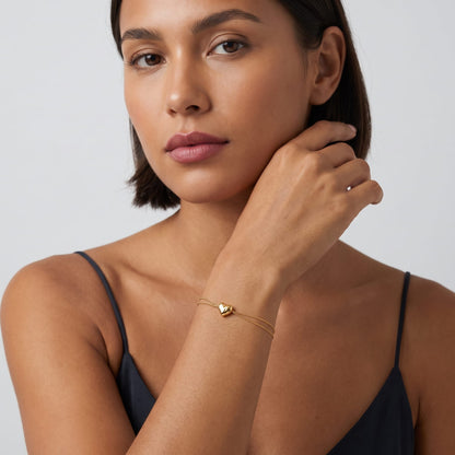 Woman wearing the Adèle hammered heart gold bracelet on the wrist posing against a neutral backdrop