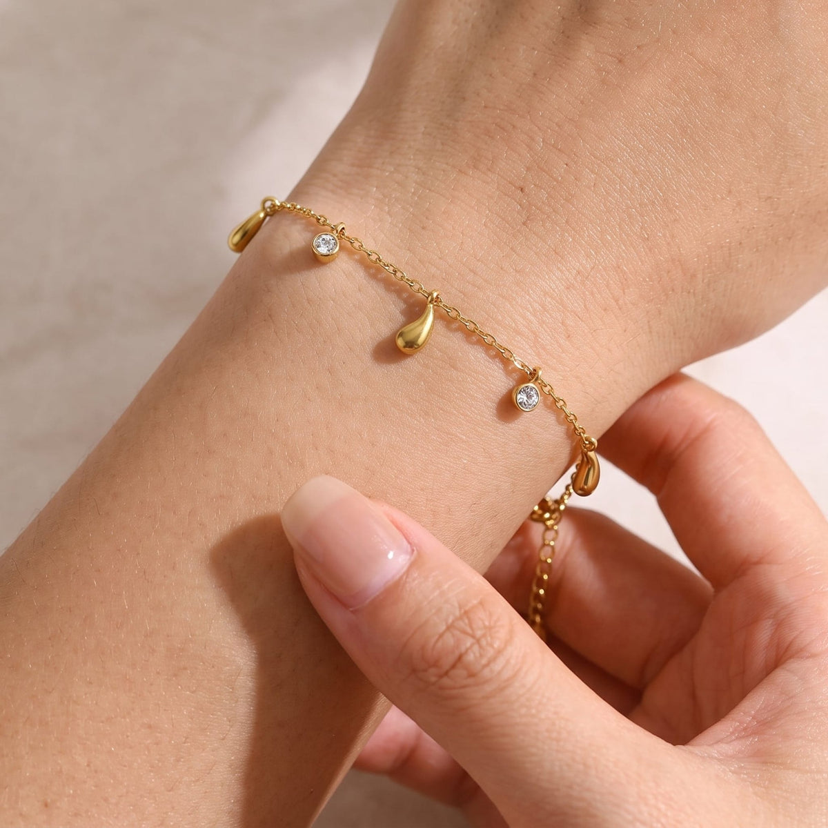 Woman wearing the Adèle gold bracelet with dangling teardrop charms and small crystal drops on the wrist