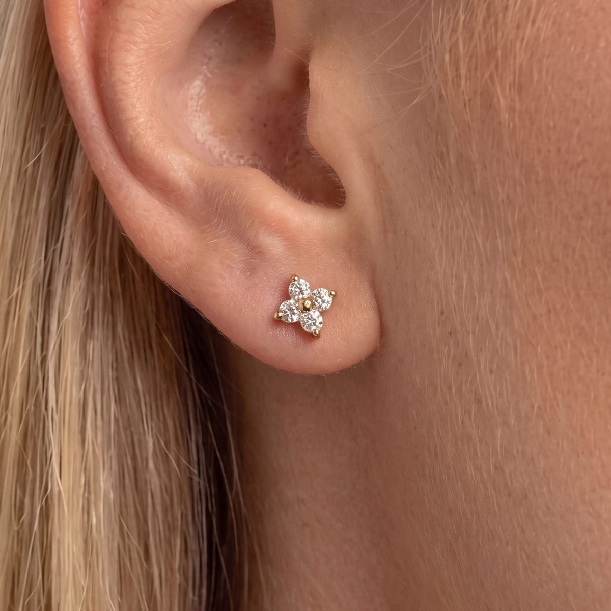 Blonde woman wearing the Agathe four-petal crystal clover stud in gold on the earlobe