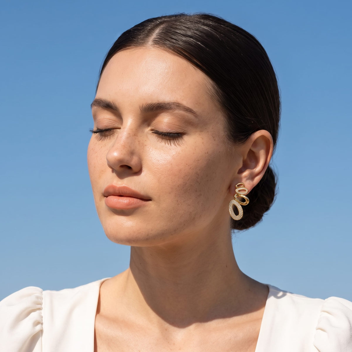 Woman wearing the Agathe pavé oval gold earrings on the ear with eyes closed in sunlight
