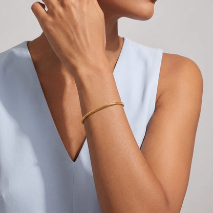 Woman in a pale blue top wearing the Alessia snake chain gold bracelet on her raised wrist