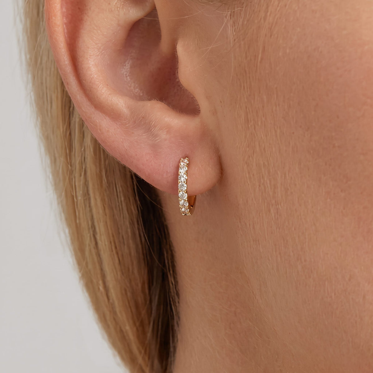 Woman wearing the slim Alexandria gold huggie lined with one row of crystals
