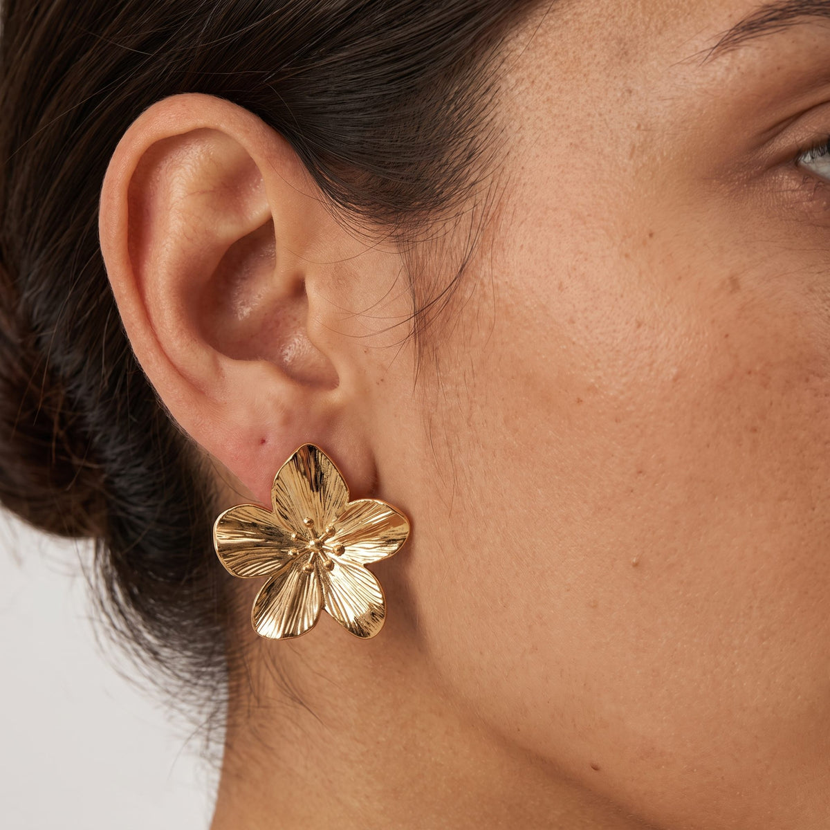 Woman with dark hair in a low bun wearing the Allysa five-petal textured gold flower earring