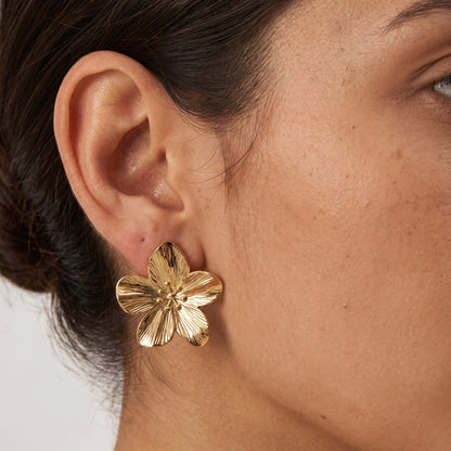 Woman with dark hair in a low bun wearing the Allysa five-petal textured gold flower earring