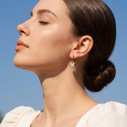 Woman wearing the Amandine hammered heart gold earrings on her ear under blue sky