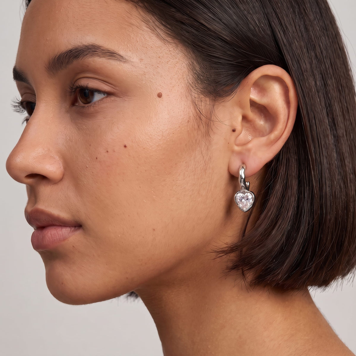 Woman wearing the Amandine hammered heart silver earrings on her ear featuring short dark hair in profile