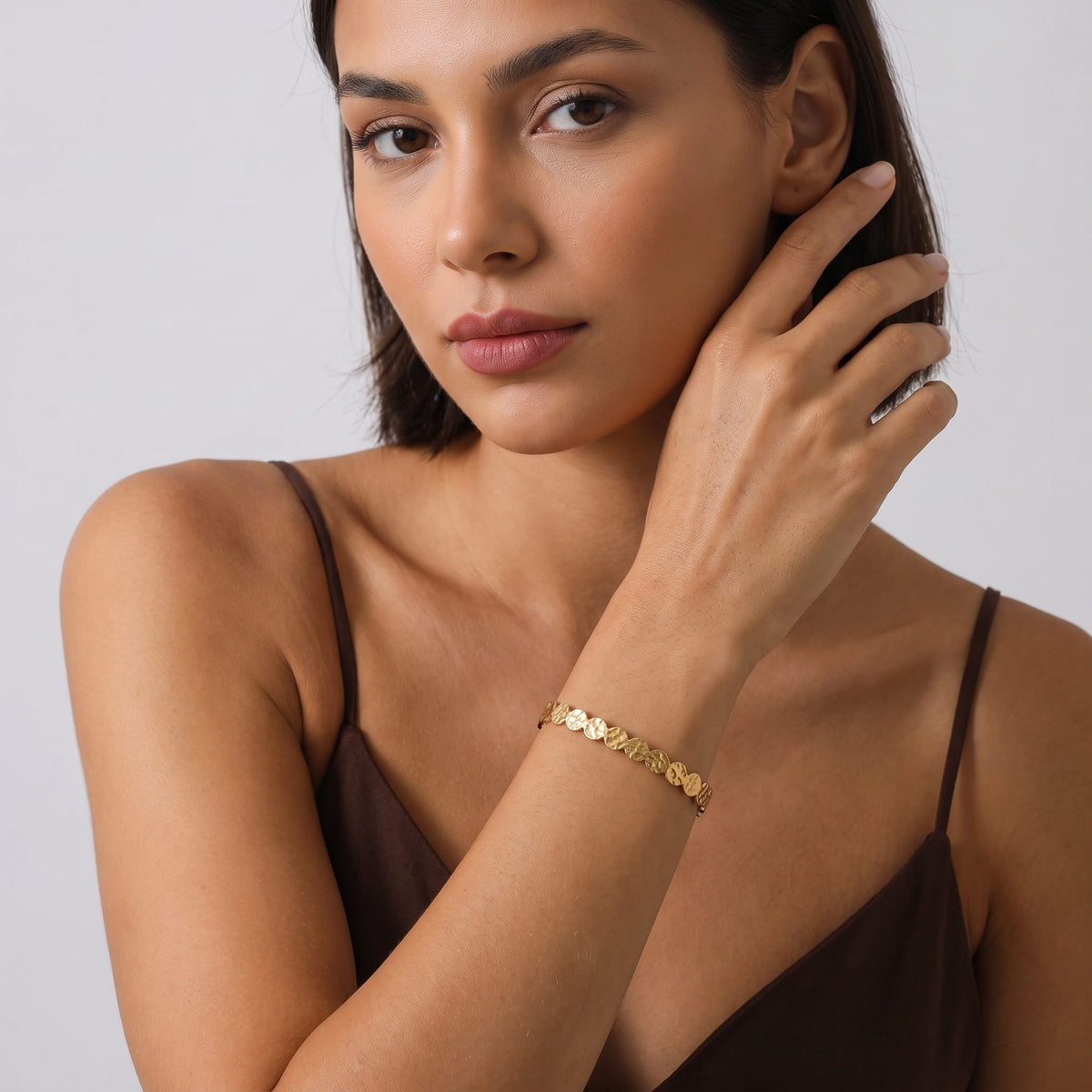 Woman wearing the Ambre hammered cuff gold bracelet on the wrist wearing a brown camisole