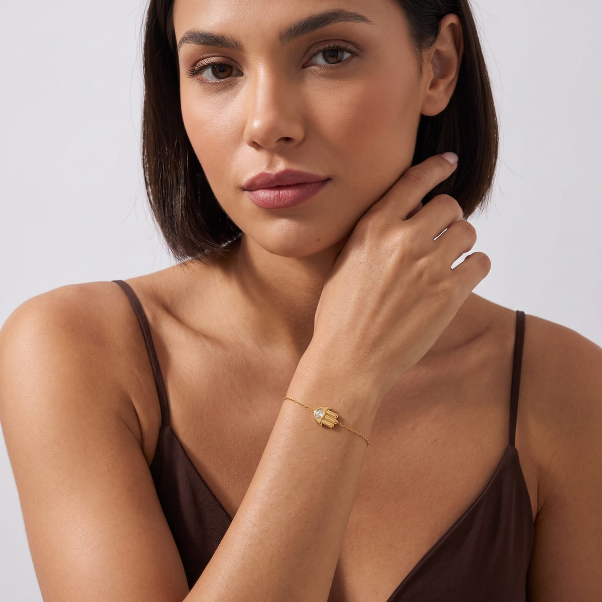 Woman wearing the Amelia crystal hamsa gold bracelet on the wrist posing in a brown tank top