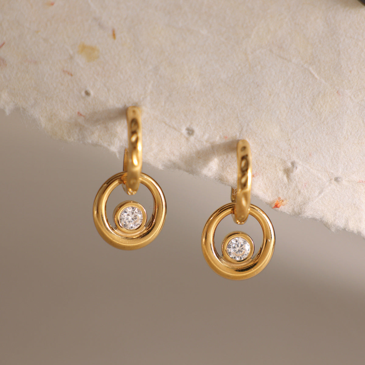 Amélie circle drop earrings hanging from a torn paper edge against a gray backdrop