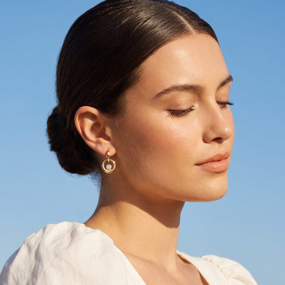 Woman wearing the Amélie circle drop gold earrings on the ear under a bright blue sky