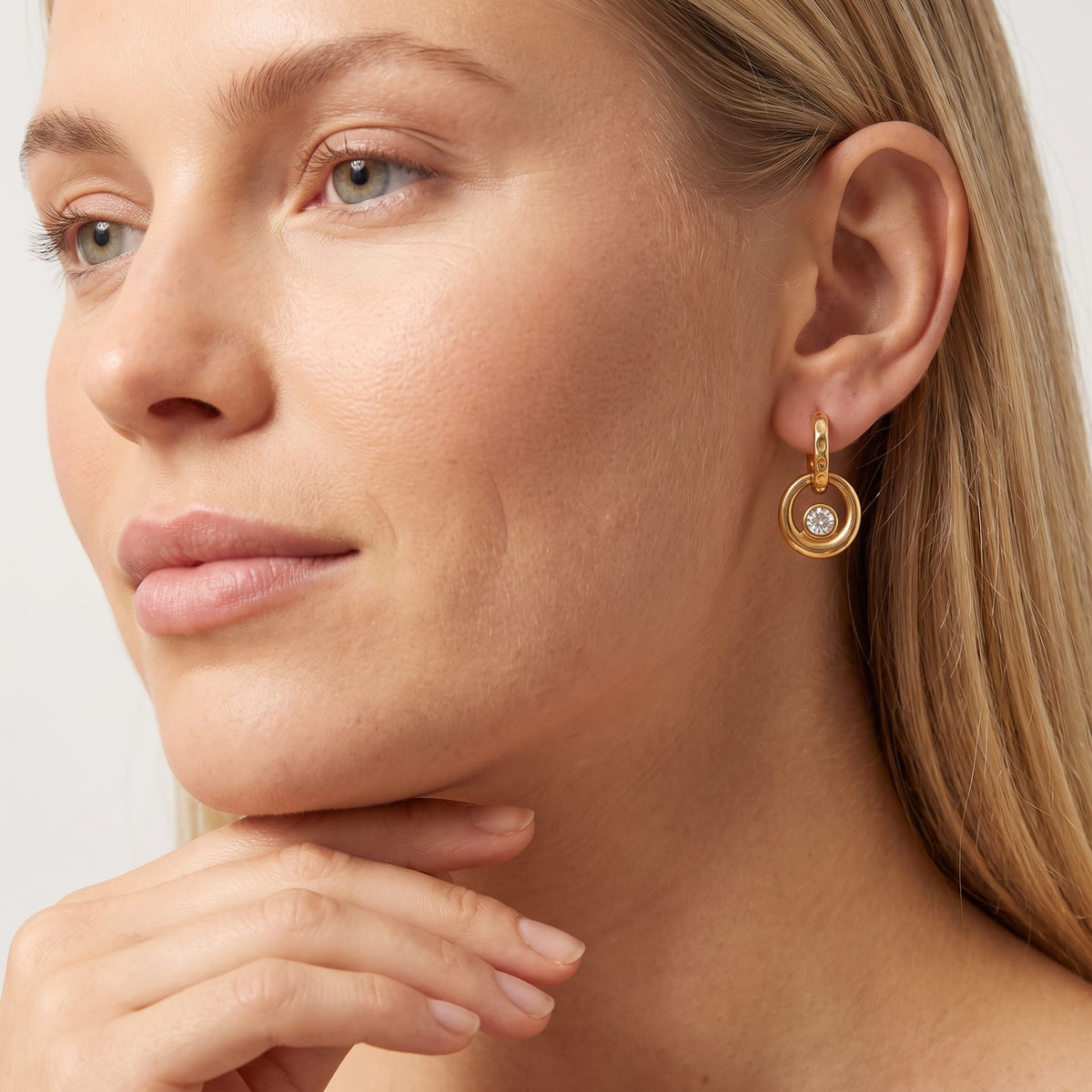 Woman wearing the Amélie circle drop gold earrings on the ear resting her chin on hand