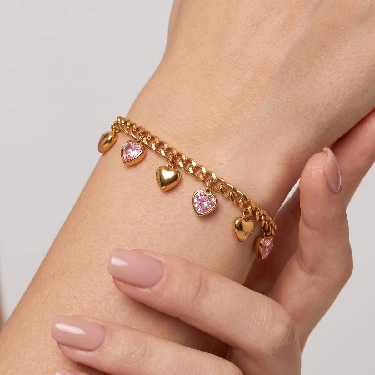 Woman wearing the Amélie heart charm gold bracelet on the wrist, with pink heart crystals