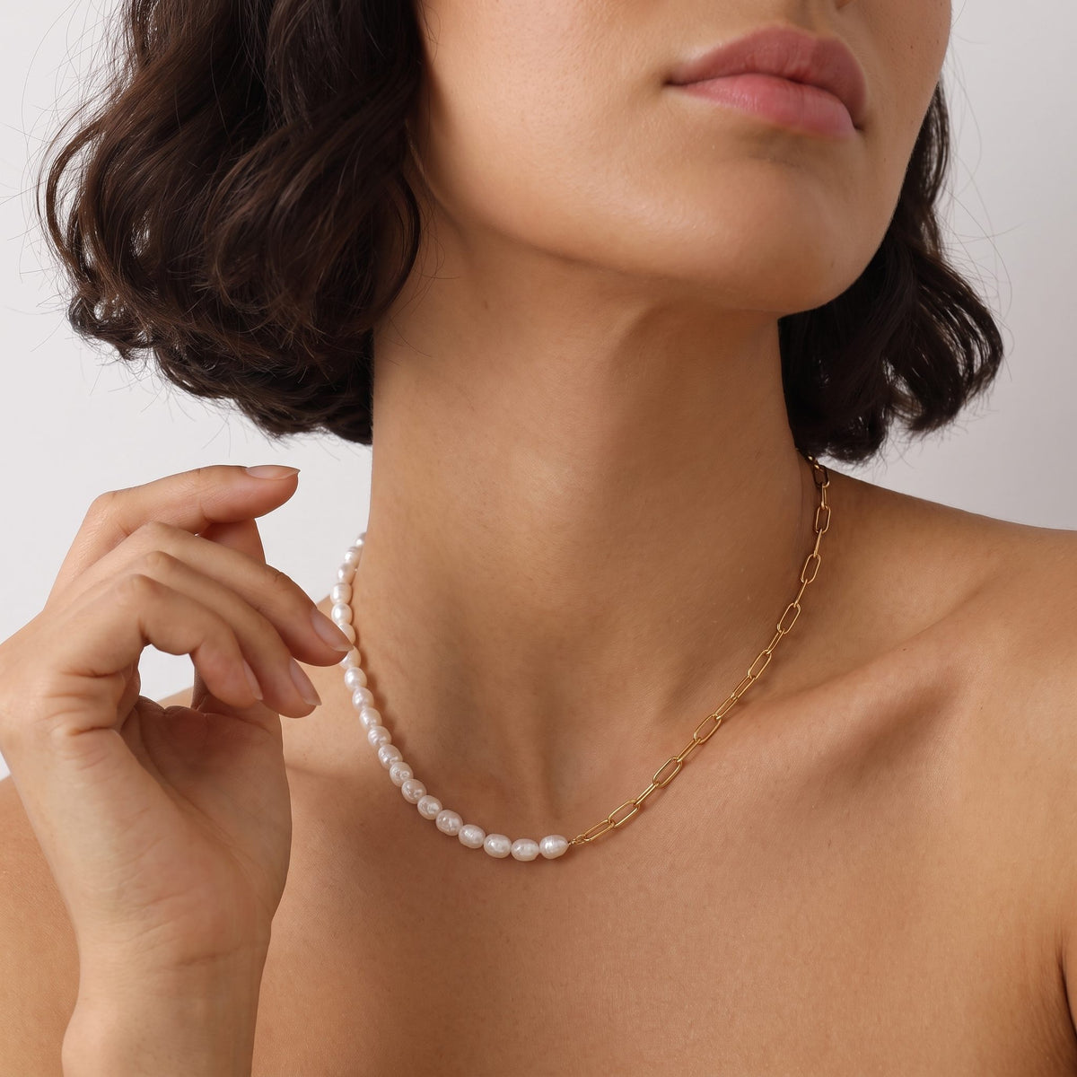 Woman with a dark bob wearing the Amélie pearl paperclip gold necklace, one hand raised near her neck