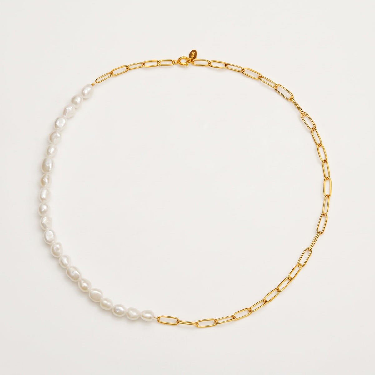 The Amélie pearl paperclip gold necklace laid flat on an off-white surface