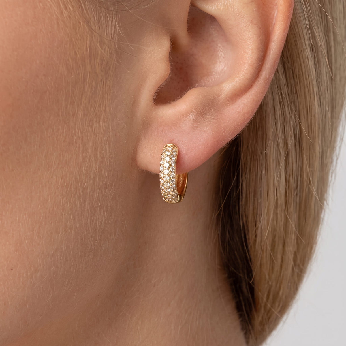 Woman wearing the Amy chunky gold huggie paved with rows of crystals