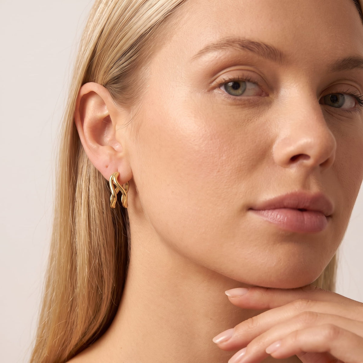 Woman wearing the Anouk double wave gold earrings on the ear resting her chin on her hand