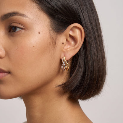 Woman wearing the Anouk double wave two-tone earrings on the ear with short dark hair