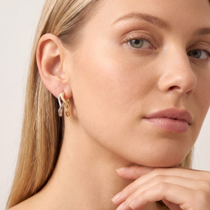 Woman wearing the Anouk double wave two-tone earrings on the ear resting her chin on hand