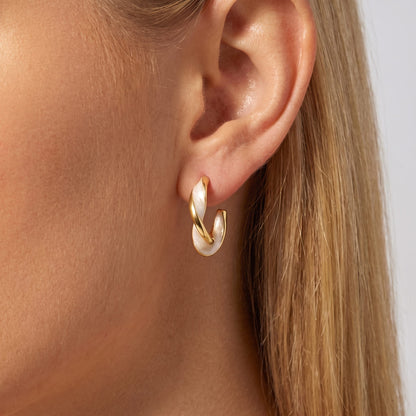 Woman wearing the Antonela twist hoop, glossy white and gold stripes spiraling around the lobe