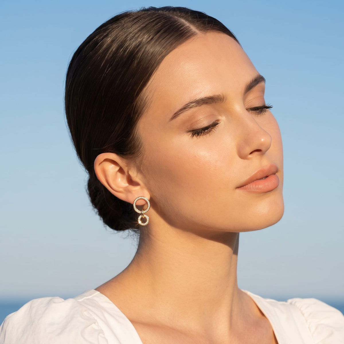 Woman wearing the Apolline double circle gold earrings on the ear against a clear blue sky