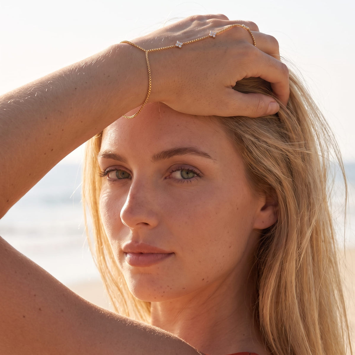 Woman wearing the Apolline hand chain gold bracelet on the hand while holding her hair outdoors