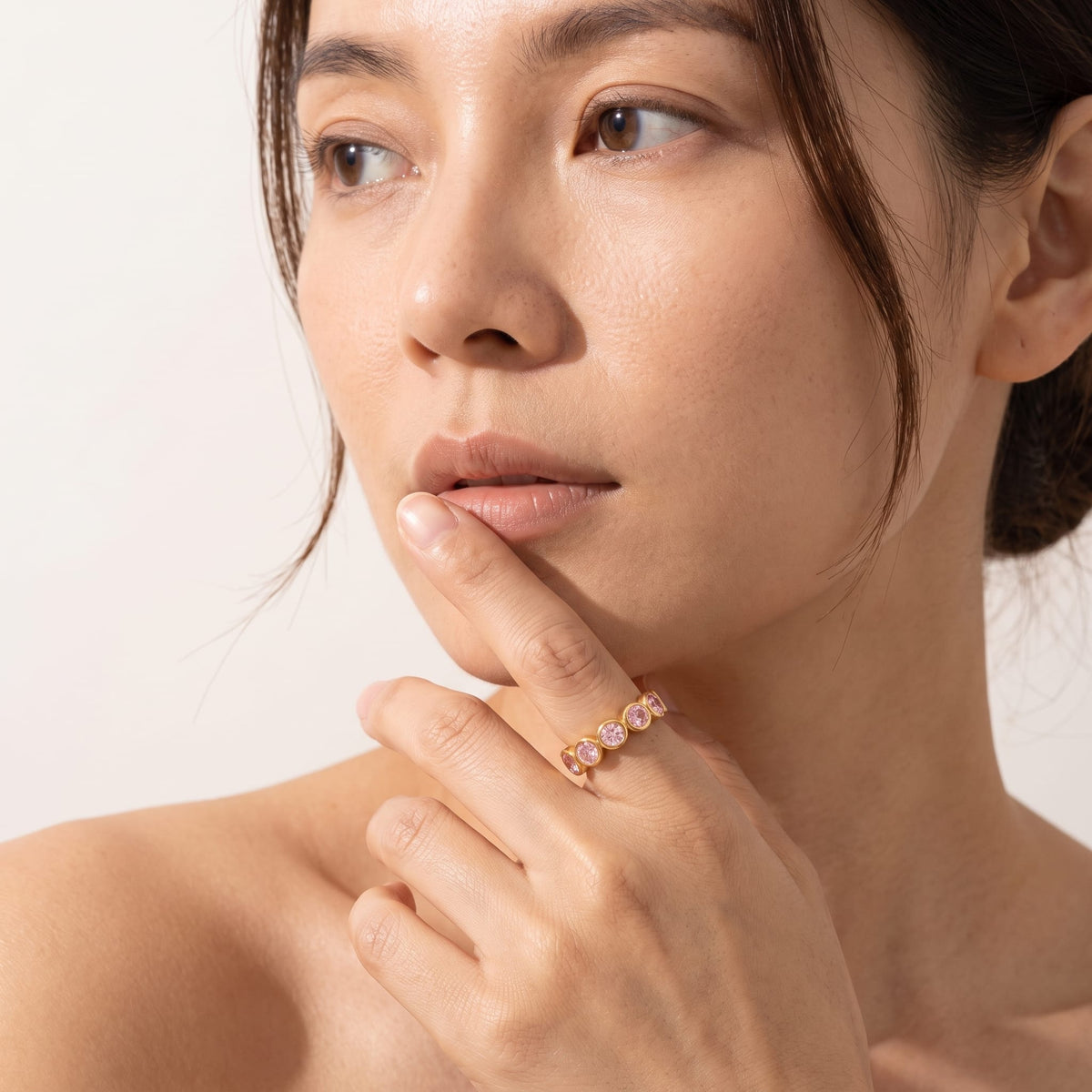 Woman wearing the Ariana pink round gold ring on the hand posed near her chin